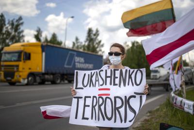 Una manifestante lleva un cartel que dice "Lukashenko = Terrorista" en una protesta contra el presidente bielorruso y en demanda de la libertad de los prisioneros políticos e Bielorrusia, cerca de Medininkai, un cruce de la frontera de Lituania con Bielorrusia, el martes, 8 de junio del 2021. (AP Foto/Mindaugas Kulbis)