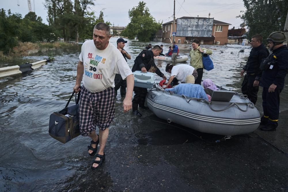 Rescue workers attempt to tow boats carrying residents being evacuated from a flooded neighborhood in Kherson, Ukraine, Tuesday, June 6, 2023. The wall of a major dam in a part of southern Ukraine has collapsed, triggering floods, endangering Europe's largest nuclear power plant and threatening drinking water supplies. (AP Photo/Libkos)