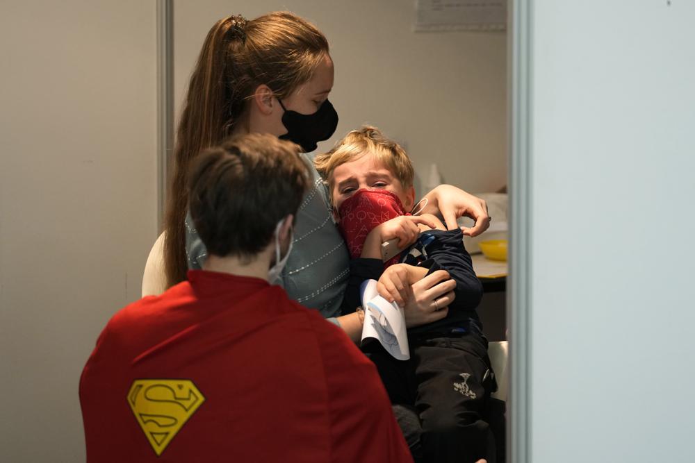 FILE- Volunteer dressed in a costume talks to a young boy who is about to receive the COVID-19 vaccine at vaccination center in Prague, Czech Republic, Saturday, Jan. 8, 2022. On Wednesday Jan. 19, 2022, the new Czech government dismissed the previous government's plan to order a vaccine mandate for the elderly people and for some professional groups. (AP Photo/Petr David Josek, File)