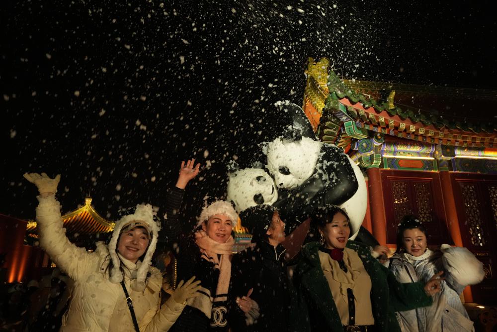 Asistentes a un evento que coincidió con la alegría de la víspera de Año Nuevo cuando una máquina de espuma vuela nieve falsa en Beijing, China, el viernes 31 de diciembre de 2021 (AP Photo / Ng Han Guan).