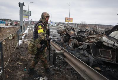 ARCHIVO - Un hombre armado junto a los restos de un vehículo militar ruso en Bucha, cerca de la capital, Kiev, Ucrania, el 1 de marzo de 2022. (AP Photo/Serhii Nuzhnenko, Archivo)