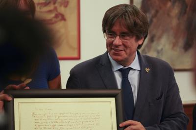 El líder separatista catalán Carles Puigdemont intercambia regalos con el alcalde de Alghero Mario Conoci (fuera de cuadro, a la izquierda) en Alghero, Italia, el sábado 25 de septiembre de 2021. (AP Foto/Andrea Rosa)