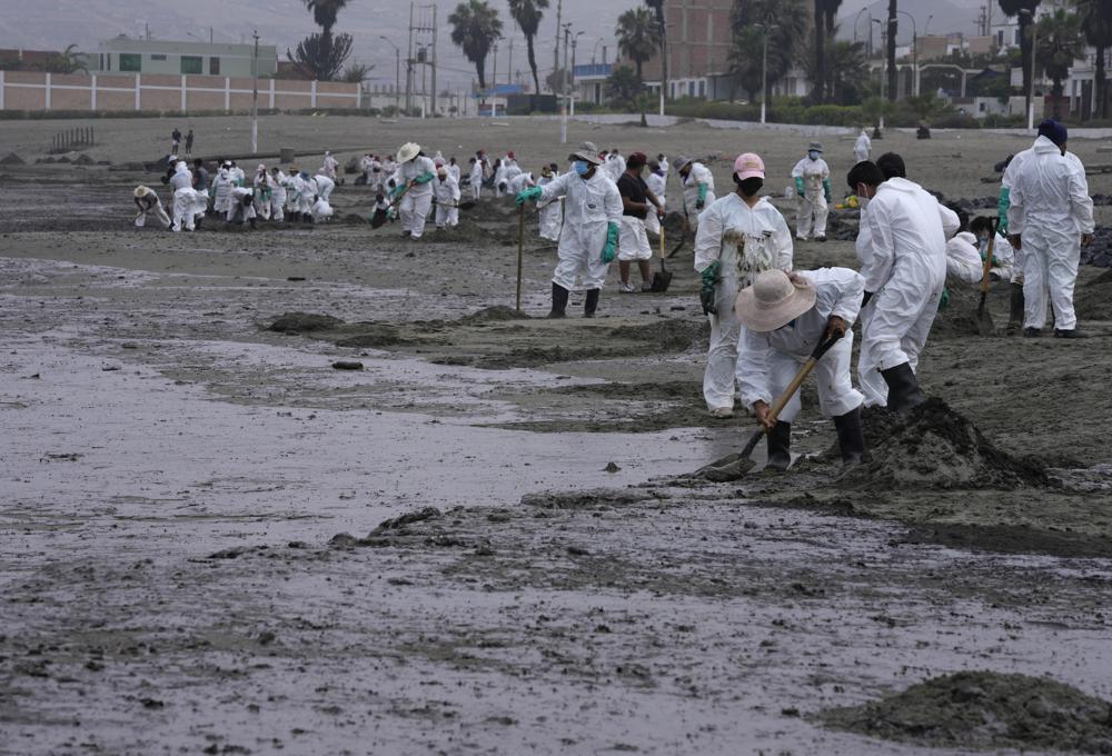 Trabajadores, vestidos con trajes protectores, continúan limpiando la playa Conchitas contaminada por un derrame de petróleo, en Ancón, Perú, el jueves 20 de enero de 2022. El derrame de petróleo en la costa peruana fue causado por las olas de la erupción de un volcán submarino. en la nación del Pacífico Sur de Tonga.  (Foto AP/Martin Mejia)