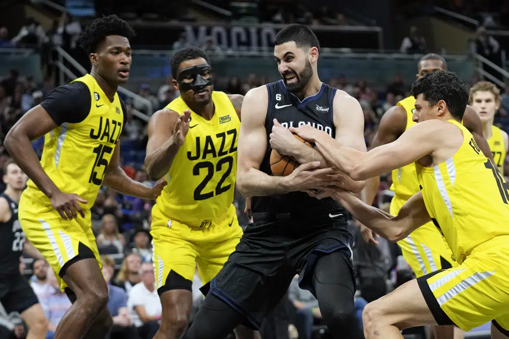 Orlando Magic's Goga Bitadze, center, struggles to keep control of the ball as he is surrounded by Utah Jazz's Damian Jones, left, Rudy Gay (22) and Simone Fontecchio, right, during the first half of an NBA basketball game, Thursday, March 9, 2023, in Orlando, Fla. (AP Photo/John Raoux)
