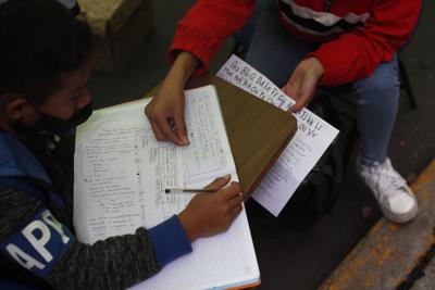 ARCHIVO - En esta fotografía de archivo del 4 de septiembre de 2020, la voluntaria Fátima Rodríguez ayuda a Bryan Quintana con su trabajo escolar frente a "Tortillerías La Abuela" en el extremo sur de la Ciudad de México. Preocupada por las dificultades educativas que enfrentan los niños durante la pandemia de coronavirus, la pareja que dirige la tortillería adaptó varios espacios fuera de su local para brindar instrucción y acceso digital a los niños de la localidad que no tienen servicio de Internet o televisión en casa, un proyecto que tiene atrajo donaciones y una lista de espera de estudiantes. (AP Foto/Rebecca Blackwell, Archivo)