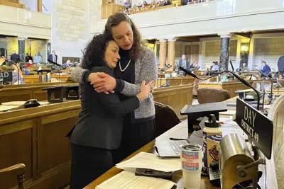 De izquierda a derecha, las senadoras de Nebraska Jen Day y Danielle Conrad se abrazan en el pleno de la legislatura estatal durante un emotivo debate sobre una propuesta de ley que prohíbe el cuidado de menores con afirmación de género, el jueves 23 de marzo de 2023 en Lincoln, Nebraska. (AP Foto/Margery Beck)
