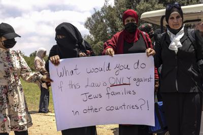 Mujeres árabes israelíes sostienen un letrero durante una protesta antes de que el parlamento de Israel vote para la renovación de una ley que prohíbe a ciudadanos árabes de Israel extender la ciudadanía o residencia a cónyuges de Cisjordania y Gaza, afuera del parlamento en Jerusalén, el lunes 5 de julio de 2021. (AP Foto/Tsafrir Abayov)