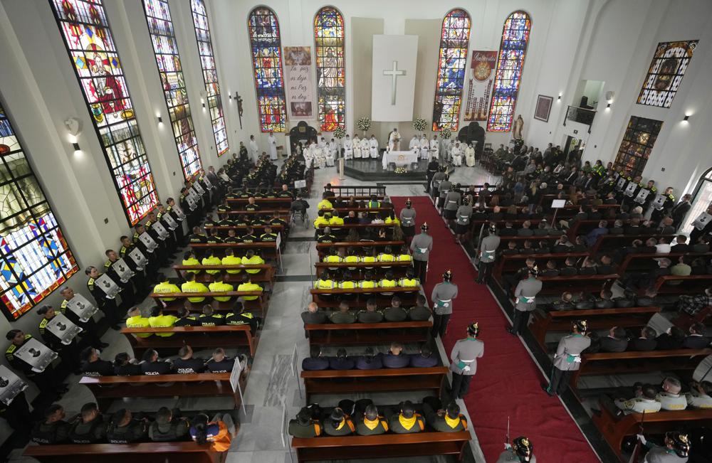 La Policía Nacional de Colombia sostiene fotos, a la izquierda, de sus colegas que fallecieron en el cumplimiento de su deber este año mientras los honran durante una misa religiosa en Bogotá, Colombia, el jueves 28 de julio de 2022. Treinta y seis oficiales caídos fueron honrados. La policía dice que fueron asesinados presuntamente por bandas criminales. (Foto AP/Fernando Vergara)