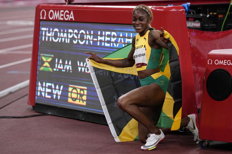 Elaine Thompson-Herah of Jamaica, poses for photographs by the clock after winning the women's 100-meters final at the 2020 Summer Olympics, Saturday, July 31, 2021, in Tokyo. (AP Photo/David J. Phillip)