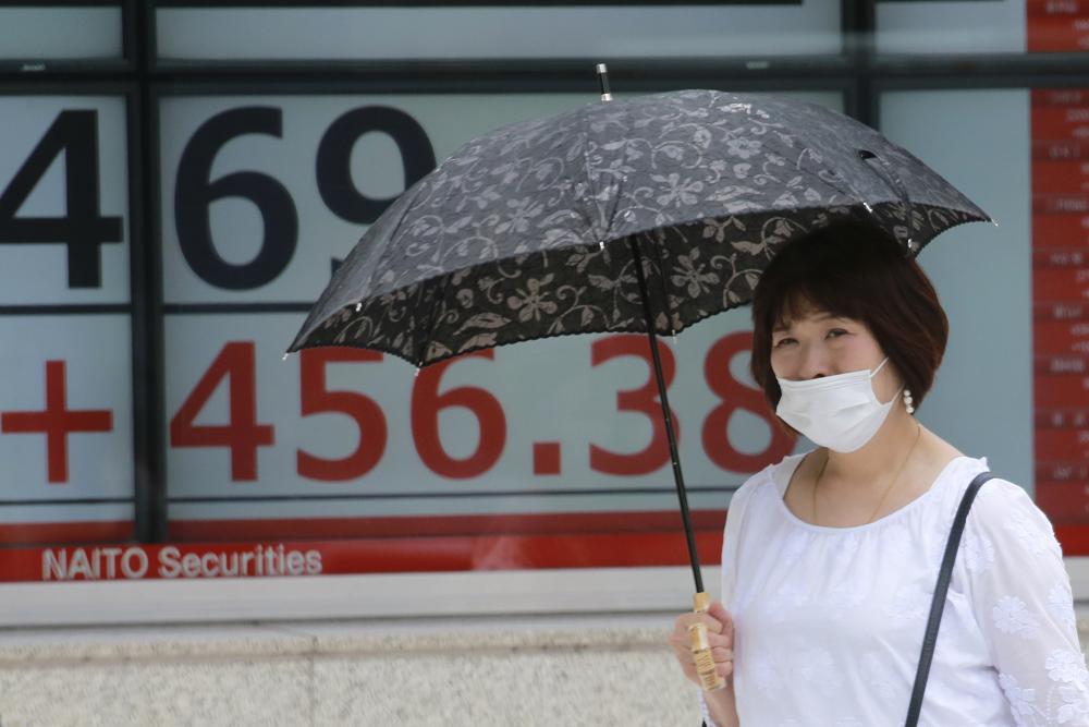 A woman walks by an electronic stock board of a securities firm in Tokyo, Monday, Aug. 23, 2021. Asian shares rose Monday as investor sentiment received a big boost from the rally last week on Wall Street, despite worries about the more contagious coronavirus delta variant not only in the region but across the world. (AP Photo/Koji Sasahara)