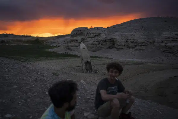 Bobby Rhinebolt, right, smokes a cigarette while sitting beside Victor Perez near a formerly sunken boat that is now above the waterline at the Lake Mead National Recreation Area, near Boulder City, Nev., on June 22, 2022. (AP Photo/John Locher)