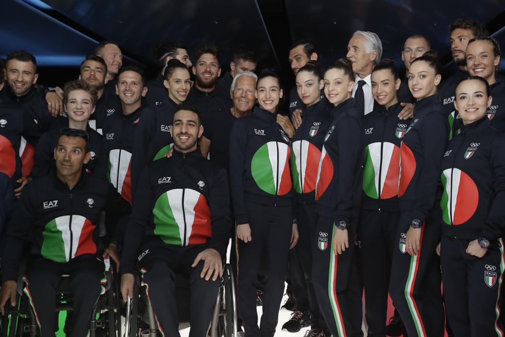 FILE - In this June 15, 2019 file photo, designer Giorgio Armani, centre, poses with Italian Olympic athletes at the end of the Emporio Armani men's Spring-Summer 2020 collection, unveiled during the fashion week, in Milan, Italy. Emporio Armani decked out Italy's team in track suits with a reinterpretation of Japan's rising sun in the colors of the country's flag: red, green and white.The Olympics in Tokyo open July 23, when the world's athletes will march behind their flag-bearers.  (AP Photo/Luca Bruno)