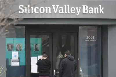 La gente mira los letreros colocados afuera de una entrada a Silicon Valley Bank en Santa Clara, California, el viernes 10 de marzo de 2023. La Corporación Federal de Seguro de Depósitos está incautando los activos de Silicon Valley Bank, marcando la mayor quiebra bancaria desde Washington Mutual durante el apogeo de la crisis financiera de 2008. La FDIC ordenó el cierre de Silicon Valley Bank e inmediatamente tomó posición de todos los depósitos en el banco el viernes. (AP Photo/Jeff Chiu)