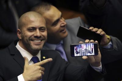 El legislador Daniel Silveira, quien fue elegido a su primer periodo representando al Partido Social Liberal, señala su teléfono con una representación del expresidente Luiz Inácio Lula de Silva durante su ceremonia de juramentación en la Cámara de Diputados en Brasilia, Brasil, el 1 de febrero de 2019. (AP Foto/Eraldo Peres, Archivo)