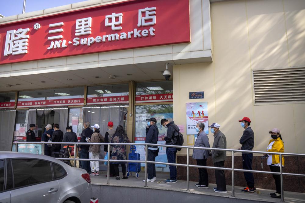 Personas con mascarillas hacen fila afuera de un supermercado en Beijing, el martes 26 de abril de 2022. Beijing realizará pruebas masivas a la mayoría de sus 21 millones de habitantes, anunciaron las autoridades el lunes, ya que un nuevo brote de COVID-19 provocó el almacenamiento de alimentos por parte de los residentes preocupados sobre la posibilidad de un cierre al estilo de Shanghái.  (Foto AP/Mark Schiefelbein)
