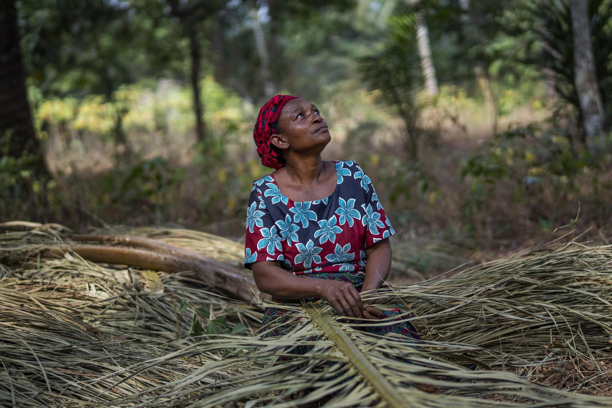 Roseline Ujah, 49, knits palm leaves in Umuida, Nigeria, Saturday, Feb. 12, 2022. Ujah's husband Godwin fell severely ill with a fever and cough. Everyone assumed at first that the palm wine tapper had contracted malaria, but then he failed to improve on medications for that disease. Doctors at a local hospital diagnosed him with COVID-19, though there were no tests available locally to confirm their suspicion. (AP Photo/Jerome Delay)