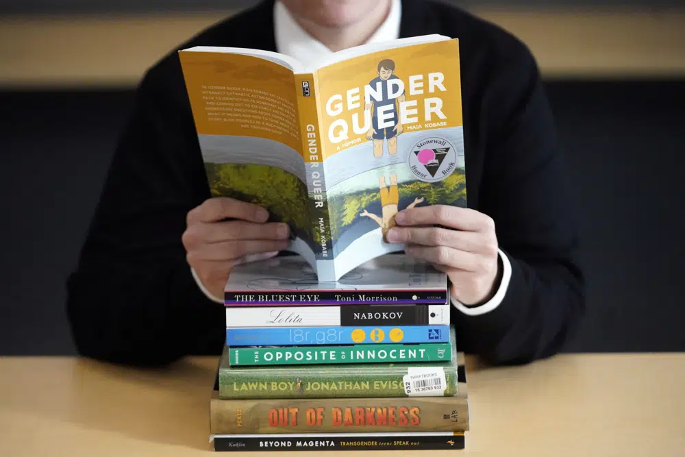 FILE - Amanda Darrow, director of youth, family and education programs at the Utah Pride Center, poses with books that have been the subject of complaints from parents in recent weeks, Dec. 16, 2021, in Salt Lake City. Books containing “sexually explicit” content — including depictions of sexual or gender identity — would be banned from North Dakota public libraries under legislation that state lawmakers heard arguments on Tuesday, Jan. 17, 2023. (AP Photo/Rick Bowmer, File)