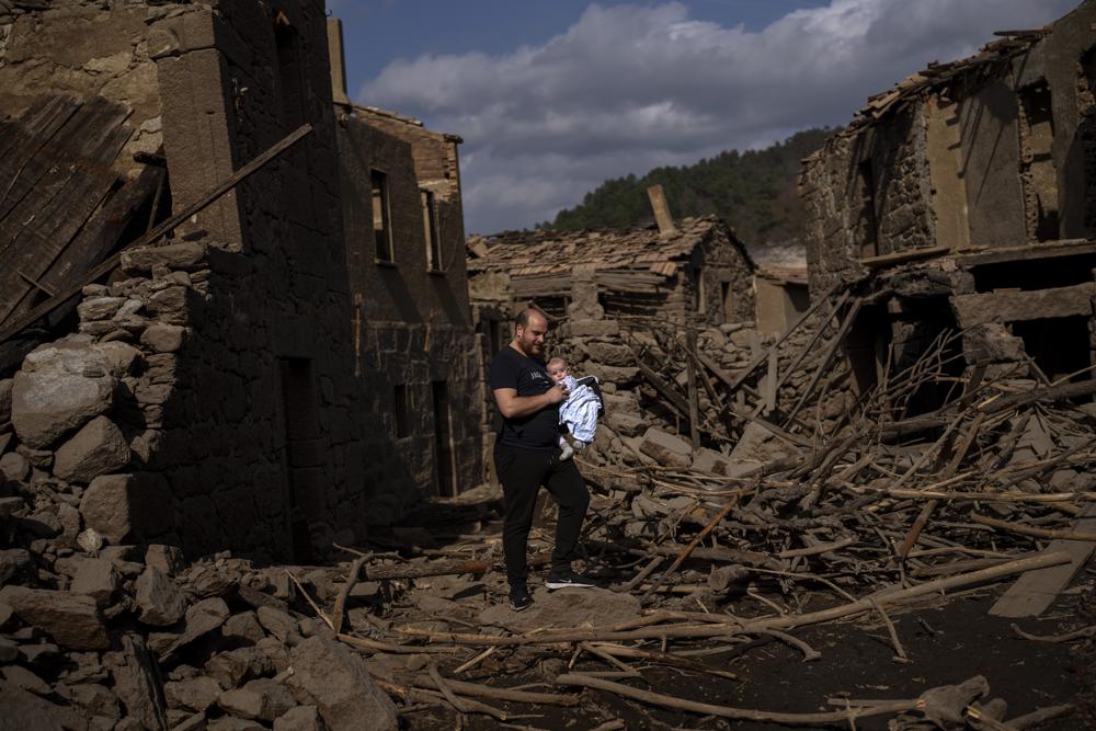 Rafael Monlina, de 33 años, sostiene a su hijo de cuatro meses, Marcos, mientras visitan el antiguo pueblo de Aceredo, sumergido hace tres décadas cuando una presa hidroeléctrica inundó el valle, emerge debido a la sequía en el embalse de Lindoso, en el noroeste de España, el sábado 12 de febrero de 2022. (AP Foto/Emilio Morenatti)