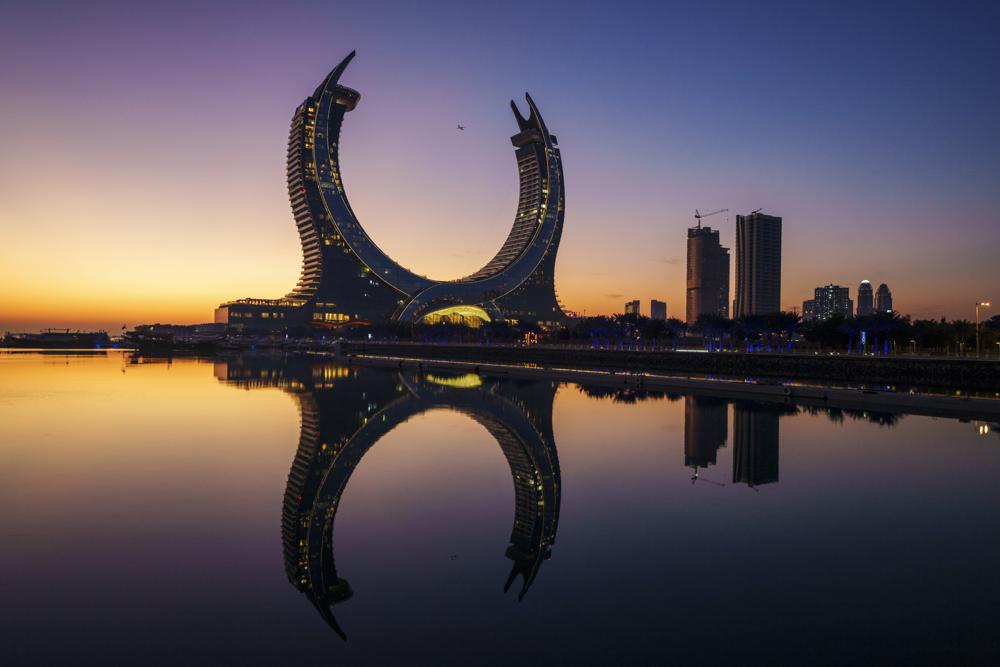 Un avión vuela entre las torres con forma de media luna de Lusail al amanecer, en Lusail, Qatar, el 24 de noviembre de 2022. (AP Foto/Pavel Golovkin)