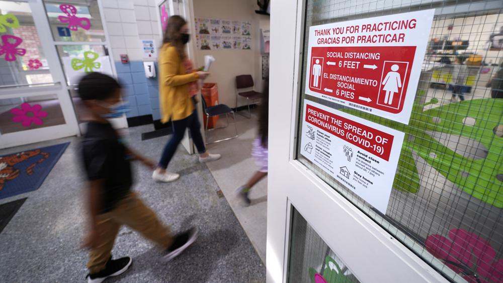 Students walk past a social distancing reminder sign while heading to the nurse's office to be tested for COVID-19, during summer school at the E.N. White School in Holyoke, Mass., on Wednesday, Aug. 4, 2021. Schools across the U.S. are about to start a new year amid a flood of federal money larger than they've ever seen before, an infusion of pandemic relief aid that is four times the amount the U.S. Department of Education sends to K-12 schools in a typical year. (AP Photo/Charles Krupa)