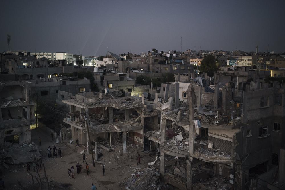 Palestinians walk at night along Al-Baali Street, next to homes heavily damaged by airstrikes during an 11-day war between Israel and Hamas, the militant group that controls Gaza, in Beit Hanoun, northern Gaza Strip, Monday, May 31, 2021. (AP Photo/Felipe Dana)