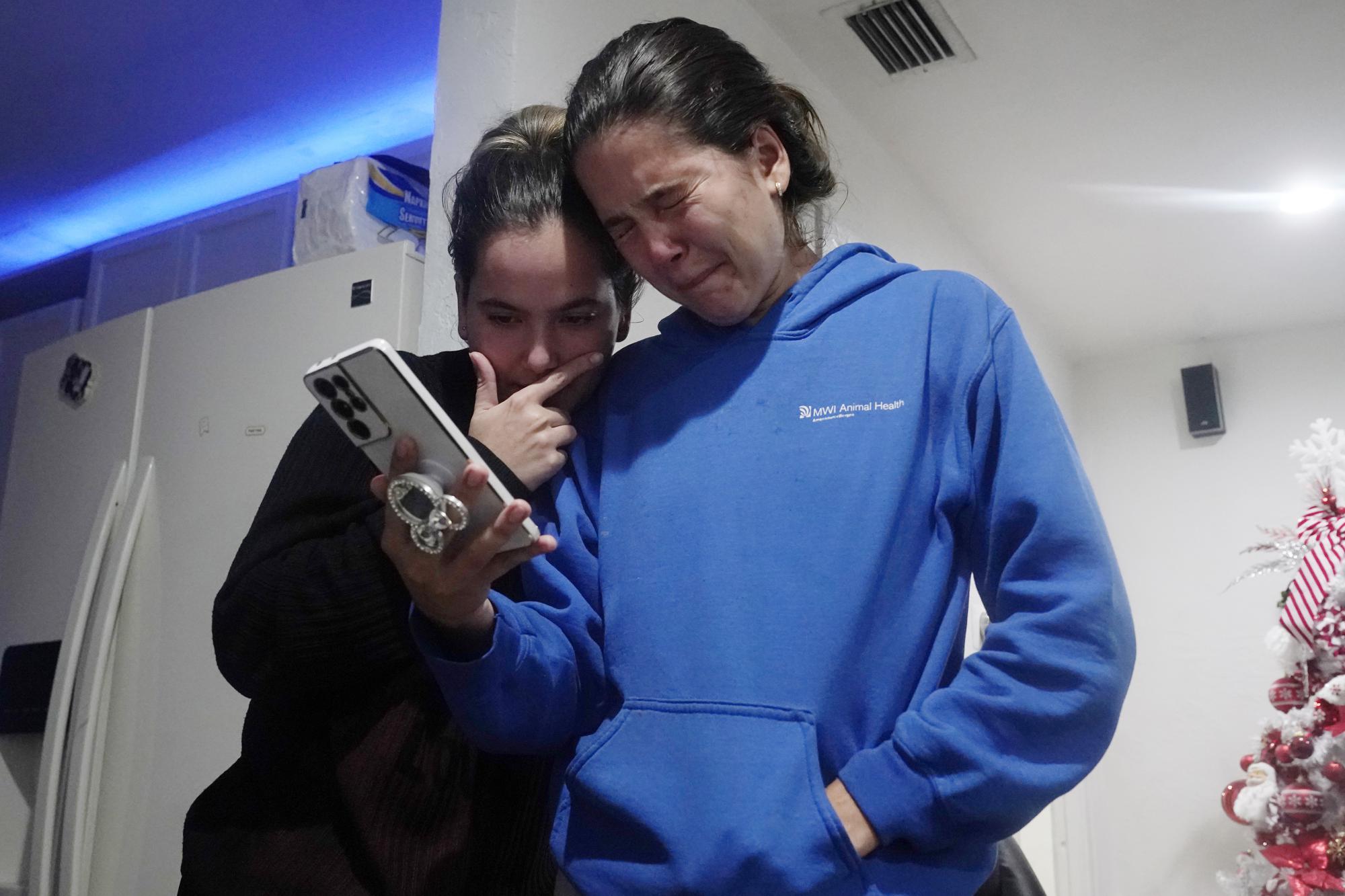 Melanie Rolo Gonzalez, right, and her sister Merlyn hold a video call with their mother and grandfather back home in Cuba, from the home of a family friend in Daytona, Florida, Tuesday, Jan. 3, 2023. On New Year's Eve, the sisters waded through the Rio Grande into the U.S., where they were immediately met by Border Patrol agents, detained and quickly released under 60 days parole. (AP Photo/Marta Lavandier)