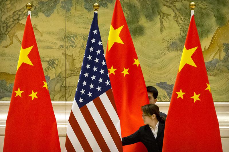 FILE - In this Feb. 14, 2019 file photo, Chinese staffers adjust U.S. and Chinese flags before the opening session of trade negotiations between U.S. and Chinese trade representatives at the Diaoyutai State Guesthouse in Beijing. For nine months under President Joe Biden, the U.S. has engaged in a diplomatic dynamic that could be characterized as about China, without China. On security, trade, climate and COVID-19, the Biden White House has tried to reorient the focus of the U.S. and its allies toward the strategic challenges posed by a rising China — all while there has been little direct engagement between the two rivals. The president is now preparing for a pair of global summits where he again won't be meeting with China’s Xi Jinping but the tensions and aggravations between the world's two largest economies will nonetheless be on ready display.(AP Photo/Mark Schiefelbein, Pool)
