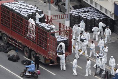 Archivo - Trabajadores con equipo de protección personal descargan comestibles de un camión antes de distribuirlos a los residentes locales en virtud del confinamiento por COVID-19 en Shanghái, China, el martes 5 de abril de 2022. (Chinatopix vía AP, Archivo)