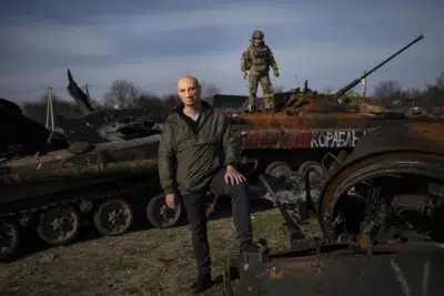 A civilian wears a Vladimir Putin mask as a spoof, while a Ukrainian soldier stands atop a destroyed Russian tank in Bucha, Ukraine, outside of Kyiv, on April 7, 2022. (AP Photo/Rodrigo Abd)