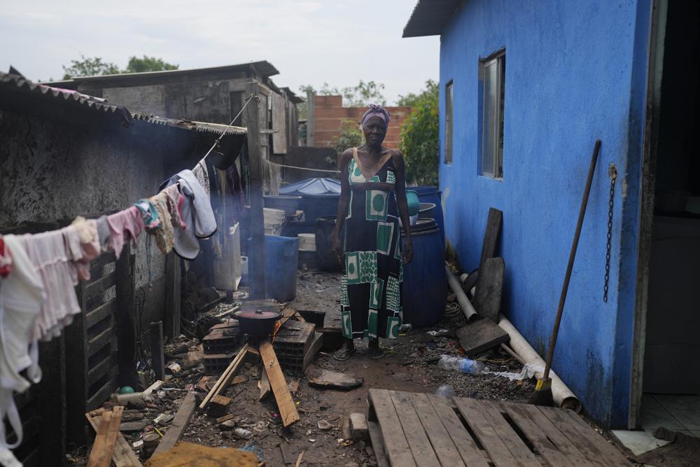 Lady Laurentino, 74, poses for a photo next a wood fire she uses to cook near the door of her home in the Jardim Gramacho favela of Rio de Janeiro, Brazil, Monday, Oct. 4, 2021.  With the surge in cooking gas prices, Laurentino says she is cooking with wood because she doesn't have money to buy another cooking gas cylinder. (AP Photo/Silvia Izquierdo)