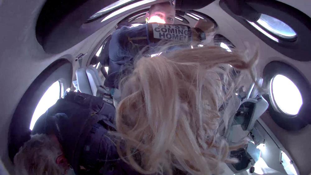 In this photo provided by Virgin Galactic, lead operations engineer Colin Bennett, top, shows a message for @England from space as he and other crew members experience zero gravity while aboard Virgin Galactic's winged rocket ship on Sunday, July 11, 2021. Entrepreneur Richard  Branson and five crewmates from his Virgin Galactic space-tourism company reached an altitude of about 53 miles (88 kilometers) over the New Mexico desert, enough to experience three to four minutes of weightlessness and see the curvature of the Earth. (Virgin Galactic via AP)