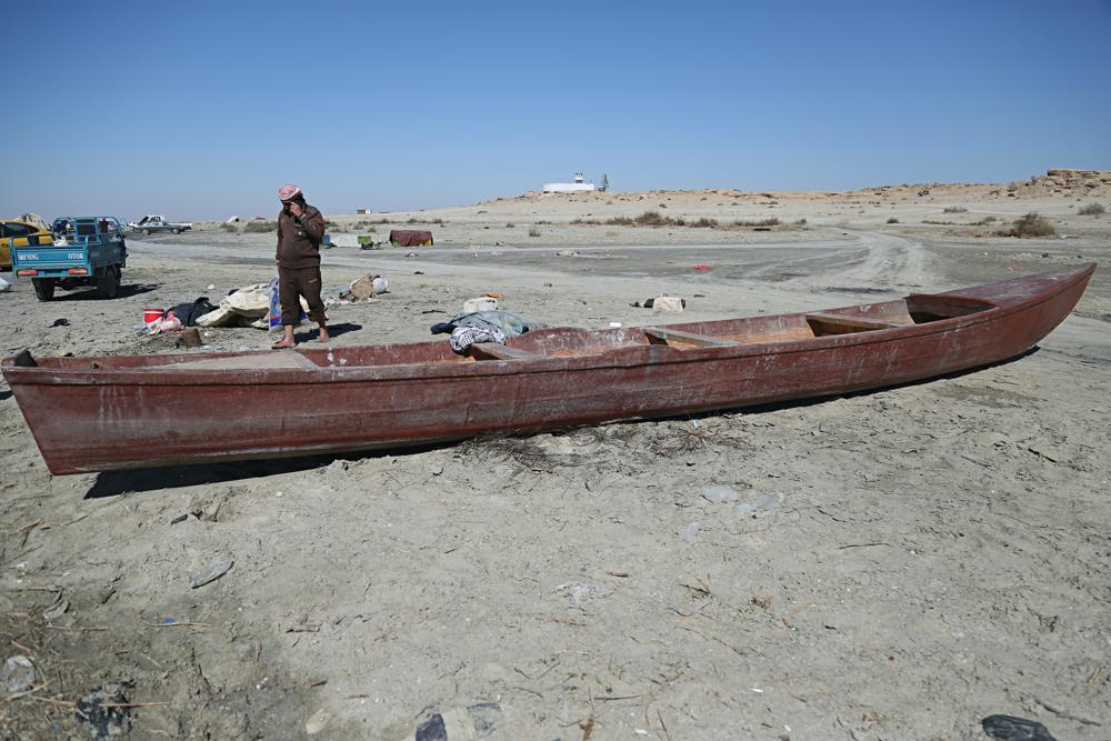 An Iraqi fisherman walks beside his boat on the banks of Razzaza Lake, also known as Lake Milh, Arabic for salt, in the Karbala governorate of Iraq, Feb. 14, 2022. The lake was once a tourist attraction known for its beautiful scenery and an abundance of fish that locals depended on. Dead fish now litter its shores and the once-fertile lands around it have turned into a barren desert. (AP Photo/Hadi Mizban)