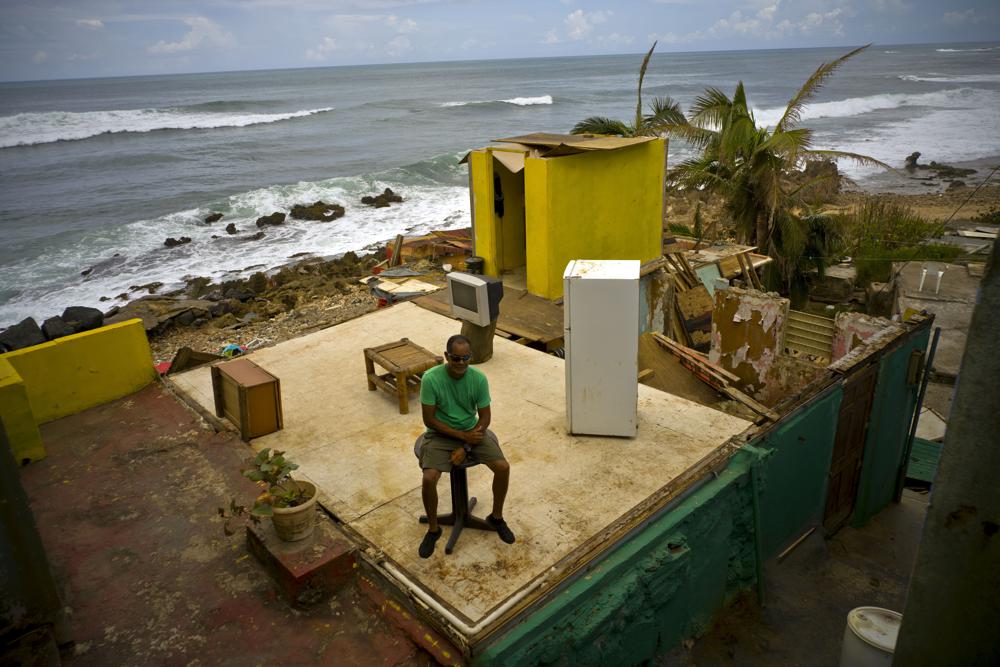 FILE - Roberto Figueroa Caballero sits on a small table in his home that was destroyed by Hurricane Maria in La Perla neighborhood on the coast of San Juan, Puerto Rico, on Oct. 5, 2017. A special United Nations panel is putting the finishing touches on a major science report that's supposed to tell people the "so what?" about climate change. The report will highlight how global warming disrupts people's lives, their natural environment and Earth itself. (AP Photo/Ramon Espinosa, File)