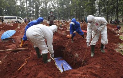 En esta imagen, tomada el 14 de julio de 2021, operarios, vestidos con trajes de protección, introducen el féretro de una víctima del COVID-19 en una tumba, en el cementerio Cipenjo de Bogor, en Java Occidental, Indonesia. (AP Foto/Achmad Ibrahim)