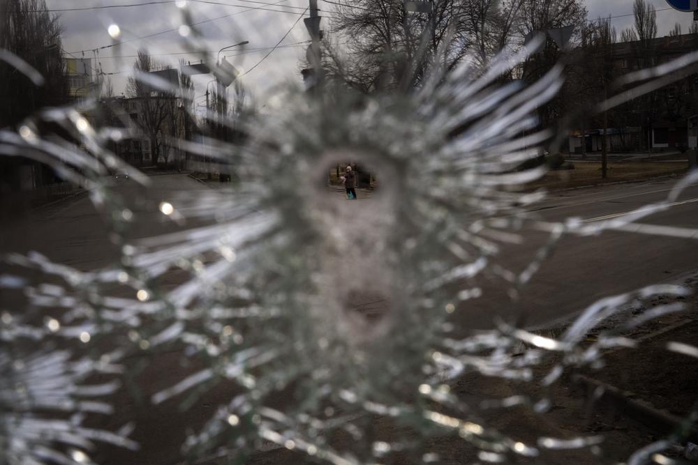 A man is seen through a bullet hole of a machine-gunned bus after an ambush in the city of Kyiv, Ukraine, Friday, March 4, 2022. While a small group of reservists were burying their comrade, 54-year-old Volodymyr Nezhenets, who was one of three killed on Feb. 26 in an ambush Ukrainian authorities say was caused by Russian 'saboteurs', a few kilometers away from the cemetery, the remains of the convoy Volodymyr was killed in 6 days ago still stands in the road with charred vehicles, a bus riddled with bullets, a spatter of blood on the drivers seat. (AP Photo/Emilio Morenatti)