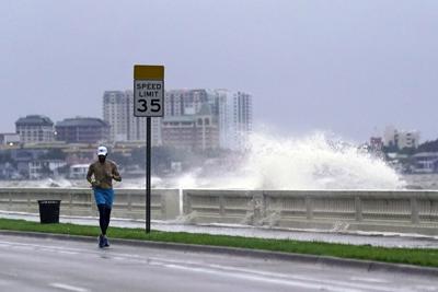 Un corredor pasa por el Bulevar Bayshore en Tampa, Florida, mientras una ola rompe sobre el muelle tras el paso de la tormenta tropical Elsa, el miércoles 7 de julio de 2021. (AP foto/John Raoux)