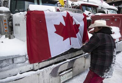 Un camionero retira una bandera de Canadá de la capota de su vehículo mientras varios camioneros se preparan para marcharse tras participar en un bloqueo en la calle Metcalfe, mientras la policía empieza a despejar las calles cerca del Parlamento y poner fin a una protesta que comenzó en contra de las vacunas obligatorias contra el COVID-19 y se convirtió en una manifestación más general contra el gobierno y una ocupación de las calles de Ottawa, Ontario, el sábado 19 de febrero de 2022. (Justin Tang/The Canadian Press via AP)