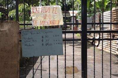 Un letrero en el que se exige el uso de mascarilla durante la pandemia de COVID-19 cuelga en un  portón a la entrada de una zona habitacional en Managua, Nicaragua, el jueves 9 de septiembre de 2021. Otros letreros anuncian la venta de cigarrillos, huevo, cerillos, leche y café. (AP Foto/Miguel Andrés)