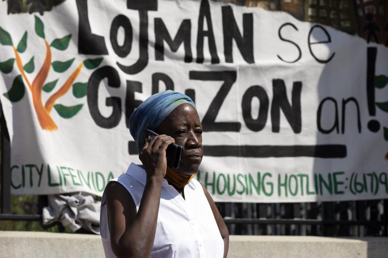 A woman speaks on the phone in front of a sign in Haitian Creole during a news conference held by a coalition of housing justice groups to protest evictions, Friday, July 30, 2021, outside the Statehouse in Boston. (AP Photo/Michael Dwyer)
