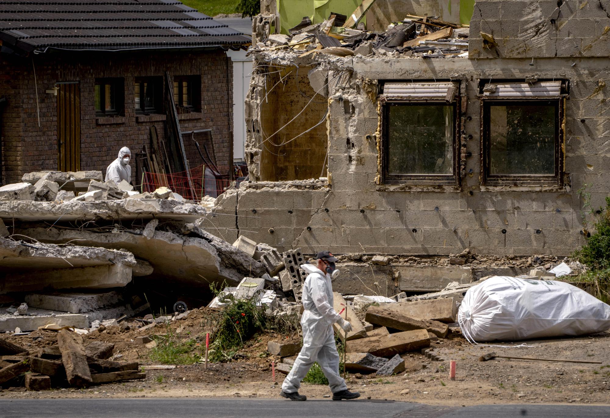 A worker walks by a home damaged from last year's floods, that is now torn down in the village of Ahrbrueck in the Ahrtal valley, Germany, Wednesday, July 6, 2022. Flooding caused by heavy rain hit the region on July 14, 2021 causing the death of about 130 people. (AP Photo/Michael Probst)