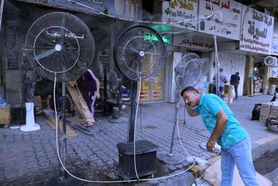 Un hombre se refresca delante de ventiladores con agua instalados en una calle de Bagdad para combatir una ola de calor, Irak, el 1 de julio de 2021. (AP Foto/Khalid Mohammed)