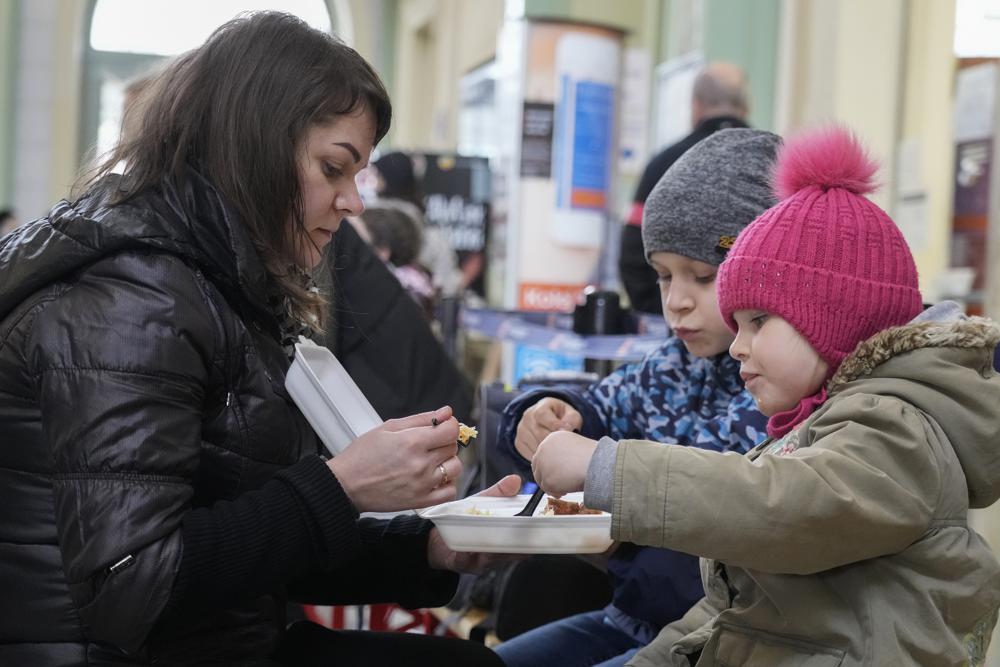 A woman and her children have a meal after fleeing the war from neighboring Ukraine at a railway station in Przemysl, Poland, on Friday, March 25, 2022. (AP Photo/Sergei Grits)