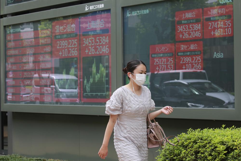 A woman walks by an electronic stock board of a securities firm in Tokyo, Monday, Aug. 23, 2021. Asian shares rose Monday as investor sentiment received a big boost from the rally last week on Wall Street, despite worries about the more contagious coronavirus delta variant not only in the region but across the world. (AP Photo/Koji Sasahara)