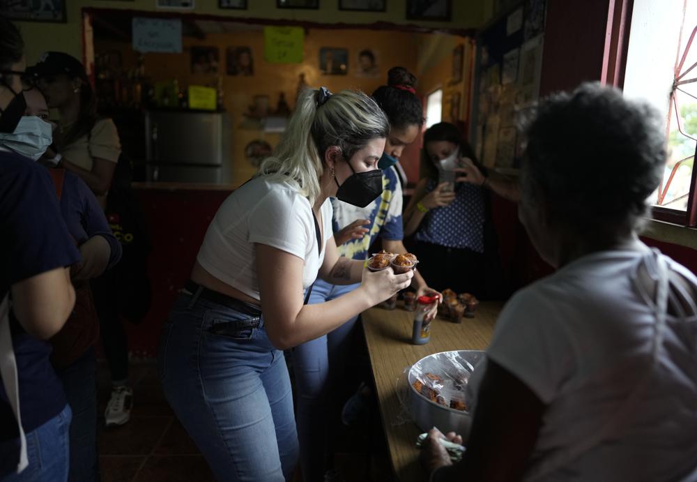 Una turista agarra un puñado de buñuelos, preparados con yuca, durante un recorrido organizado por Cumbe Tour, en el barrio San Agustín de Caracas, Venezuela, el sábado 21 de agosto de 2021. Cumbe Tour trae a turistas, extranjeros y nacionales, a San Agustín para mostrarles cómo viven los venezolanos de menores ingresos en lo que solía ser uno de los barrios más peligrosos de la ciudad. (Foto AP/Ariana Cubillos)