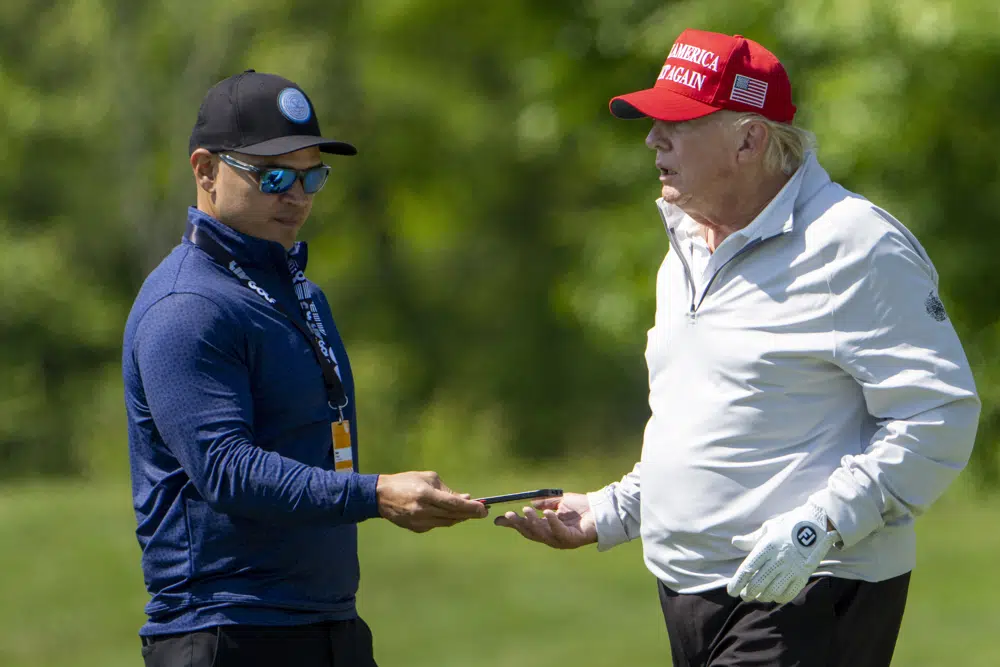 Walt Nauta, a la izquierda, toma un teléfono del expresidente Donald Trump durante el LIV Golf Pro-Am en el Trump National Golf Club, el jueves 25 de mayo de 2023, en Sterling, Virginia. Cuando Trump comparezca ante un tribunal federal en Miami, es probable que ser acompañado en el banquillo de los testigos por un hombre con mucha práctica para estar a su lado: auta, su ayuda de cámara convertido en cómplice.  (Foto AP/Alex Brandon, archivo)