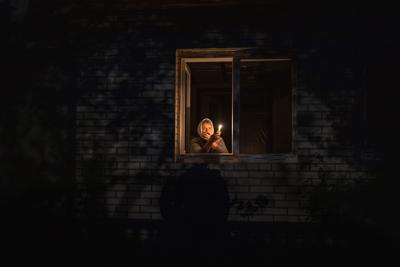 Catherine, de 70 años, mira por la ventana mientras se ilumina con una vela dentro de su casa durante un apagón, el jueves 20 de octubre de 2022, en Borodyanka, en la región de Kiev, Ucrania. (AP Foto/Emilio Morenatti)