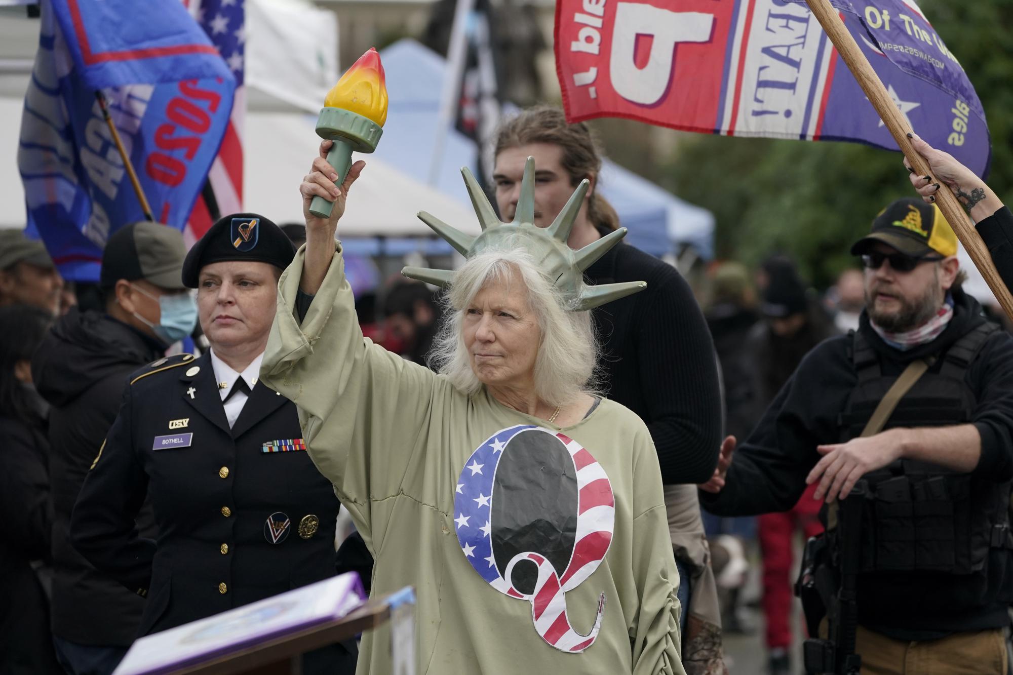 FILE - In this Wednesday, Jan. 6, 2021 file photo, a person dressed as "Lady Liberty" wears a shirt with the letter Q, referring to QAnon, as protesters take part in a protest at the Capitol in Olympia, Wash., against the counting of electoral votes in Washington, DC, affirming President-elect Joe Biden's victory. Twenty years on, the skepticism and suspicion first revealed by 9/11 conspiracy theories has metastasized, spread by the internet and nurtured by pundits and politicians like Donald Trump. One hoax after another has emerged, each more bizarre than the last: birtherism. Pizzagate. QAnon. (AP Photo/Ted S. Warren, File)