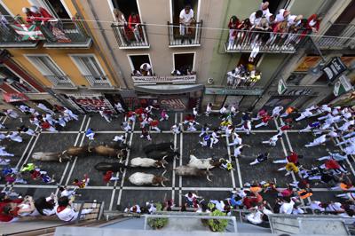 People run in the street with fighting bulls and steers during the running of the bulls at the San Fermin Festival in Pamplona, northern Spain, Sunday, July 10, 2022. Revellers from around the world flock to Pamplona every year for nine days of uninterrupted partying in Pamplona's famed running of the bulls festival which was suspended for the past two years because of the coronavirus pandemic. (AP Photo/Alvaro Barrientos)
