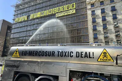 Un activista de Greenpeace rocía agua para simular pesticida hacia el edificio del Consejo Europeo, donde están reunidos los ministros de comercio de la UE en Bruselas, jueves 25 de mayo de 2023. La leyenda en el camión dice "UE-Mercosur acuerdo tóxico". (AP Foto/Sylvain Plazy)