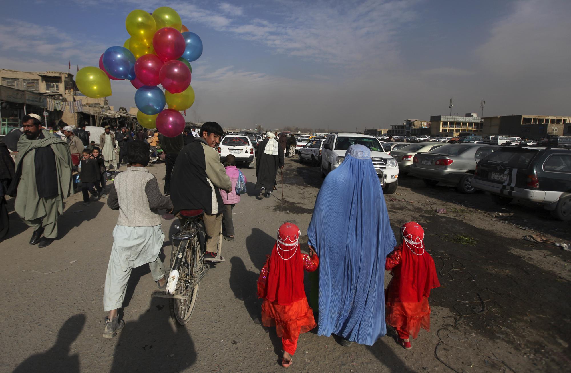 FILE - In this Jan. 3, 2011 file photo, a balloon seller riding a bicycle looks towards a woman holding hands with two young girls at a market in Kabul, Afghanistan. (AP Photo/Altaf Qadri, File)